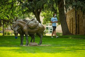 Masked student walks by A Friend to Lean on statue