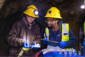 Two students in hardhats look at sample in mine