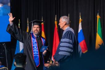 Student waves while walking across the stage at commencement