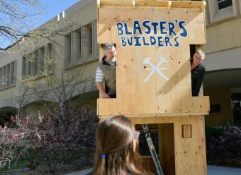 People peek out the windows of the Blaster's Builders two story wood building