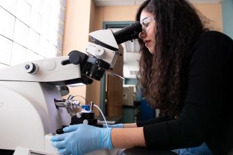 Female student looks through microscope in lab