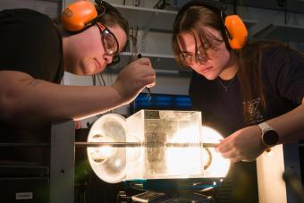 two female students wearing orange ear protectors conduct experiment