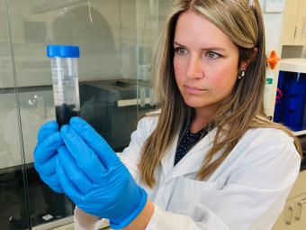 lori tunstall in white lab coat and blue gloves holding a test tube