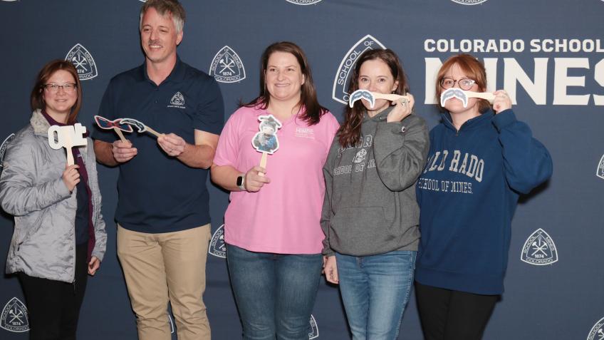 Mines faculty pose with photo props in front of Mines banner