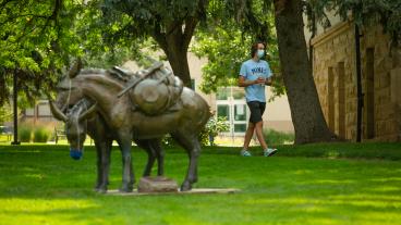 Masked student walks by A Friend to Lean on statue