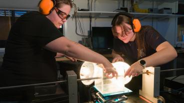 Two students in orange hearing protection perform experiment