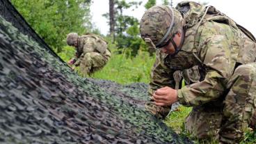 U.S. Army soldiers  weave cords through the camouflage net in order to keep their radar and area of operation concealed 