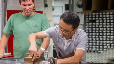 Brandon Dugan (Co-Chief Scientist, Colorado School of Mines, USA) watches Tao Yang (Paleomagnetist, Institute of Geophysics, China Earthquake Administration, China) at the core sampling table. (Credit: Tim Fulton, IODP-JRSO)